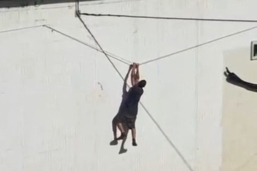 pendurado-em-fiacao,-homem-escala-muro-do-buraco-do-tatu-e-foge-da-pm.-veja-video