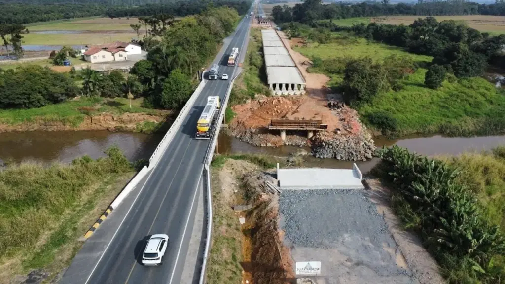 Nova ponte de 510 metros na BR-280 recebe 12 vigas de 55 toneladas em operação especial entre Guaramirim e Araquari, com sistema pare e siga durante quatro dias, enquanto guindastes posicionam peças de 28 metros que fazem parte de uma estrutura prevista para reunir 108 vigas sobre o rio Piraí