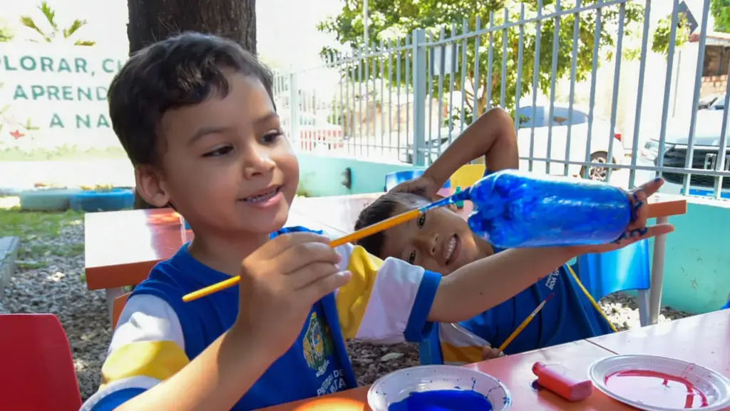 Crianças da Escola Municipal Vovó Clara, em Boa Vista, pintam e reaproveitam garrafas PET para criar telhado e dar sombra ao parquinho; projeto escolar surpreende entre 150 selecionados do Prêmio Nacional Liga STEAM 2026
