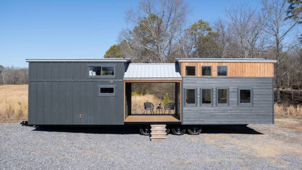 Minicasa sobre rodas de 42 m² usa varanda central para separar sala, cozinha e quartos, mede 13,7 metros de comprimento e acomoda até quatro pessoas com dormitório principal, home office, banheiro completo e mezanino, adotando solução que faz o projeto compacto parecer um verdadeiro chalé de campo