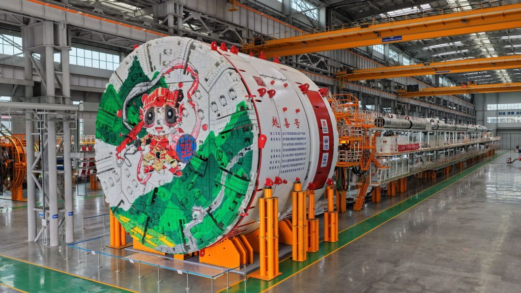 Monstro de 3.500 toneladas e 220 metros, mais comprido que dois campos de futebol, sai da fábrica na China para abrir um túnel de 18 km dentro da montanha com guia a laser que erra no máximo 3 milímetros na medição